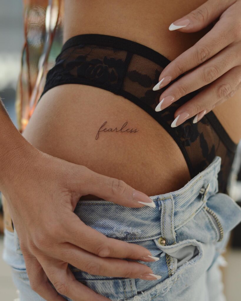 'Fearless' Fineline Text Script Lettering Tattoo on the Hip, a Bold Proclamation: Fearless Expression 