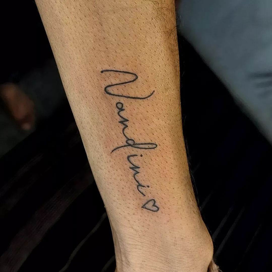 woman's wrist with cursive script tattoo and an open heart