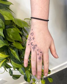 This may contain: a person's hand with stars and moon tattoos on their left wrist, next to a potted plant