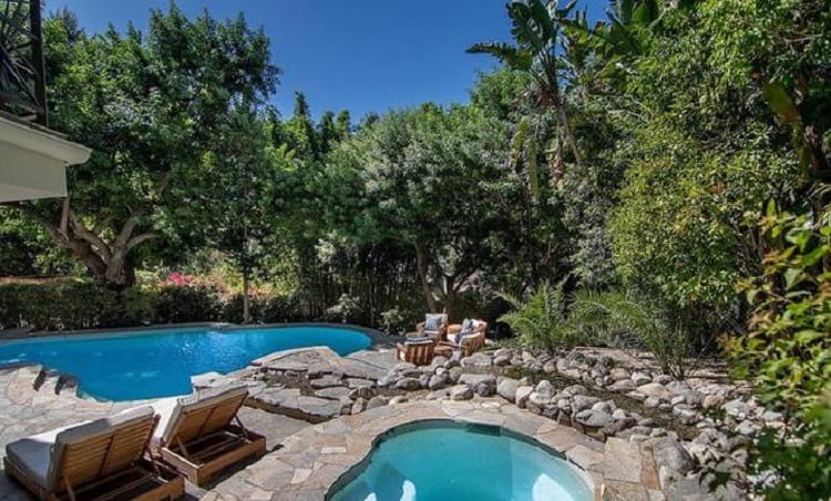 Outdoor area with a pool, spa and seating, surrounded by lush trees and greenery