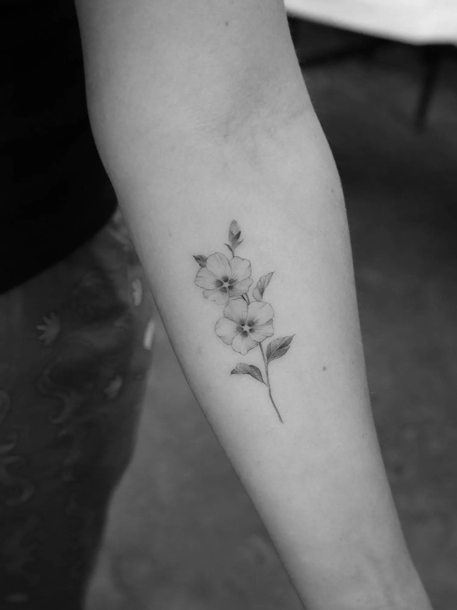 black and white close up photo of black ink tattoo of two flowers on forearm